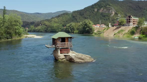 Aerial Shot Which a Small House Stands on a Rock in the Middle of the River alt