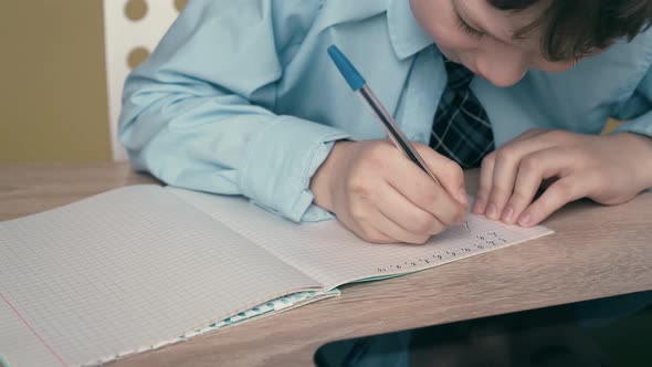 Ext CU, Tracking: Schoolboy Does Homework, Writes a Pen in a Notebook, on the Table Is a Tablet. alt