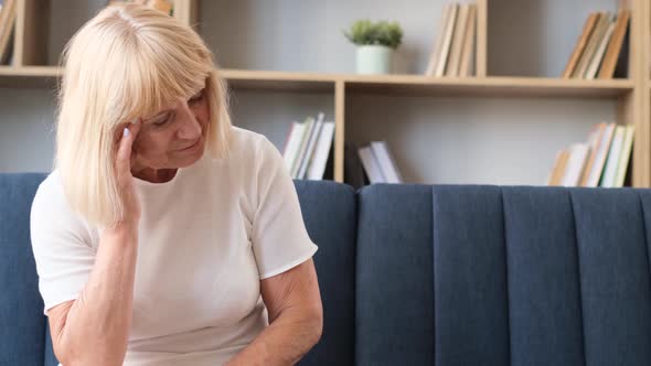 Portrait of Grayhaired Grandmother Suffering From Pain and Migraine Retired Woman Sitting on Sofa alt