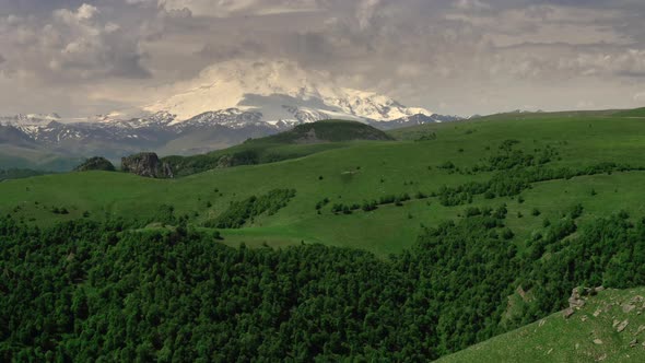 Mount Elbrus and green hills at sunny summer day.
