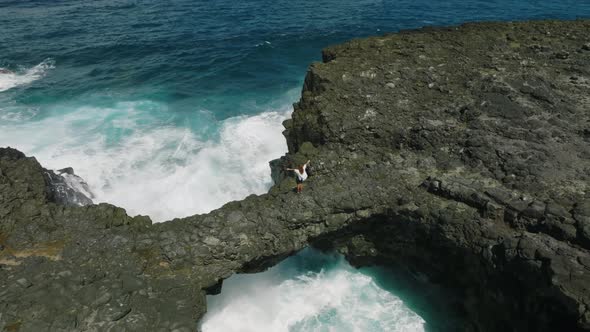 A Young Girl in a White Dress Stands on the Rocks on the Shore of the Indian Ocean alt