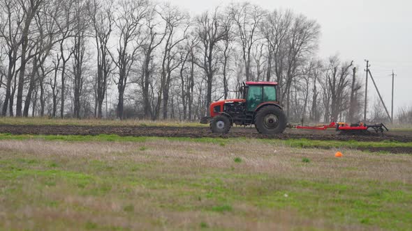 Tractor with Harrow System Plowing Ground on Cultivated Farm Field Pillar of Dust Trails Behind alt