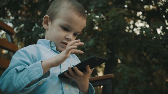 Little Boy Playing Video Games on His Smartphone Outdoors. alt