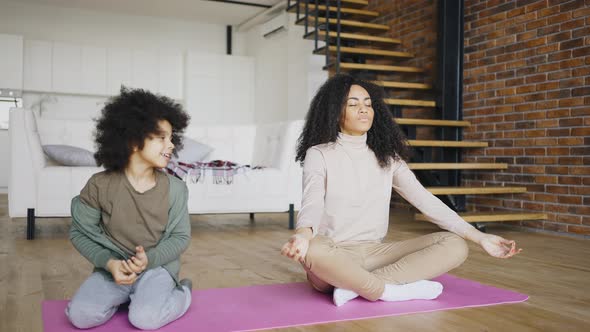 Mixed Race Mother and Son Doing Meditation Sitting on a Carpet on the Floor of Their House alt