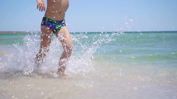Little Boy Runs Along a Sandy Beach on a Sunny Summer Day Raising Spray