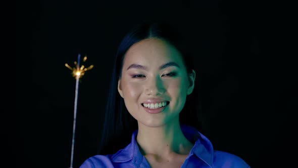 Portrait Of Smiling Beautiful Asian Woman With Sparkler In Hand alt