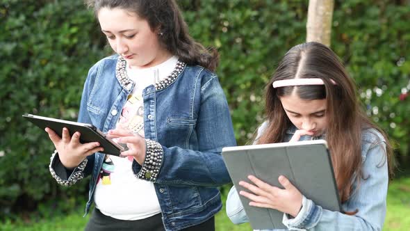 Two Young Girls Relaxing Outdoor Playing with Tablet alt