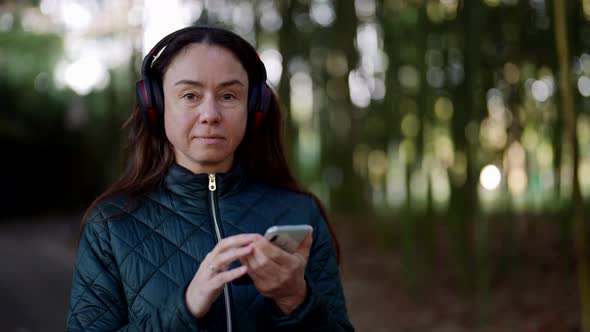 Portrait of a Pretty Adult Woman with Wireless Headphones Standing in a Park and Listening to Music alt