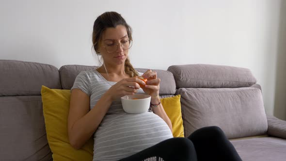 Beautiful pregnant woman with glasses peals tangerine and eats it alt