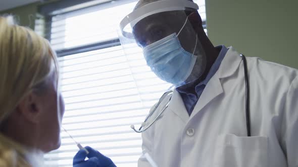 Diverse female patient and doctor wearing face mask doing covid swab test alt