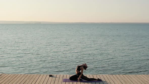 Woman Practicing Yoga in Pigeon Pose Sitting on Sport Mat on River Wooden Pier.
