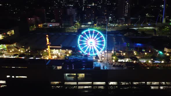 Side aerial view of an amusement park at night with lights and people enjoying alt