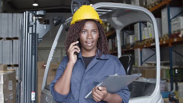 Excited Female Factory Employee in Helmet Talking on Phone