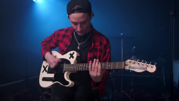 A Man in a Shirt Plays an Electric Guitar in a Music Studio Against a Background of Blue Neon Lights