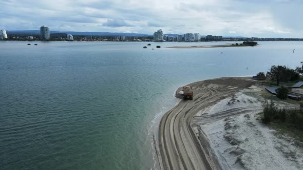 Highing drone view following a large dump truck carrying sand along a coastal beach road. alt