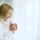 Beautiful Blonde Woman Looking out Curtained Window and Drinking Coffee - VideoHive Item for Sale