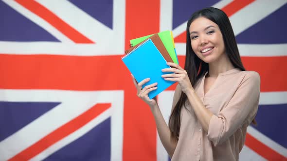 Pretty Female Student Showing Copybooks Against British Flag, Learning Language alt