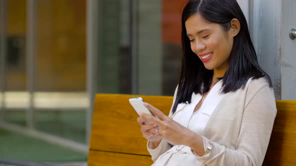 Asian Woman Using Smartphone Sitting on Bench alt
