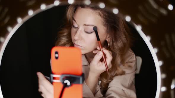 Attractive Female Makeup Artist Applies Eyeshadow Sitting in Front of Ring Light