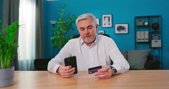 Mature 50s Man Sit at Table Use Smart Phone Makes Purchase on Internet Ecommerce Retail alt