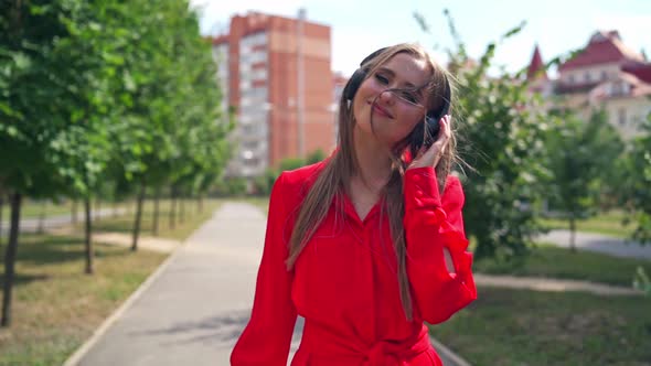 Beautiful young woman with headphones. Happy girl walking and enjoying listening to music alt