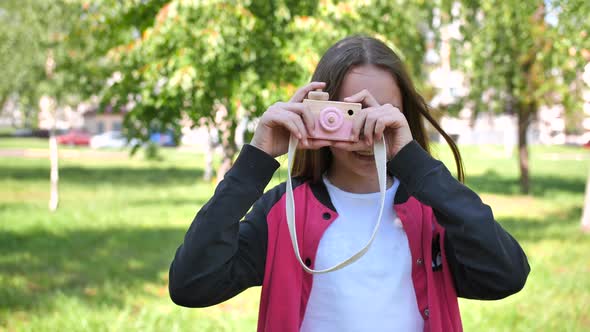 Girl 11 Years Old Takes Pictures with a Toy Wooden Pink Camera. alt