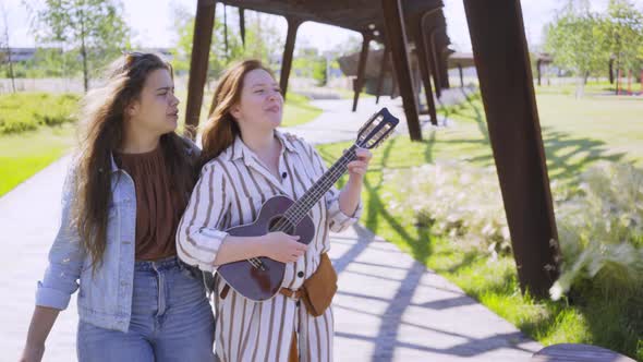 Woman Hugs Friend Playing Ukulele in Contemporary City Park
