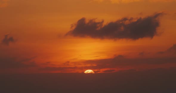 Orange warm sunset time lapse with big sun hiding behind clouds alt