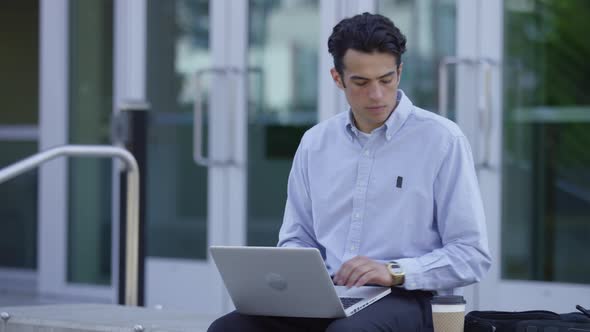 Young businessman using laptop and drinking coffee outdoors