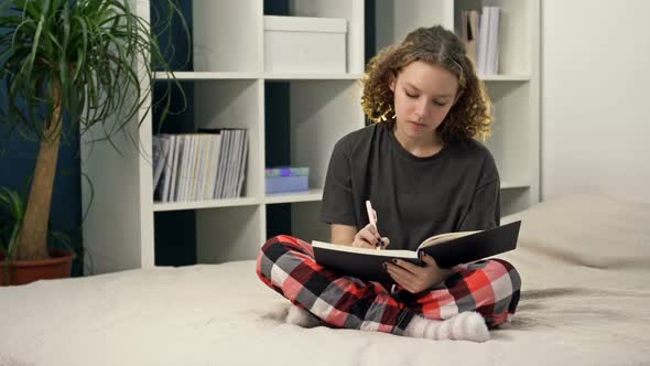 Cute Teenage Girl Doing Homework Sitting on the Bed at Home