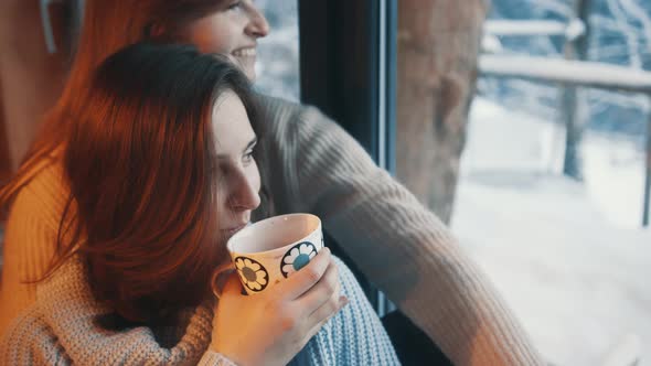 Two Fashionable Beautiful Lesbian Girls are Sitting Near the Window and Drinking Coffee alt