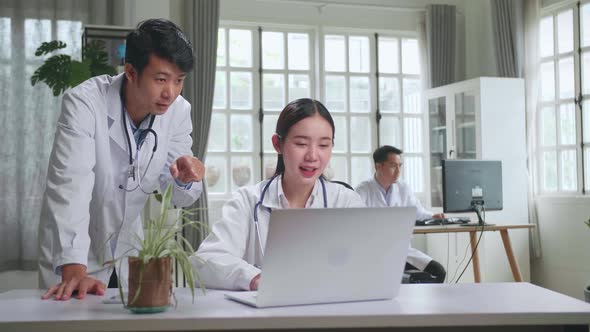 Two Asian Professional Physicians Talking, Consulting And Working On Laptop Computer alt