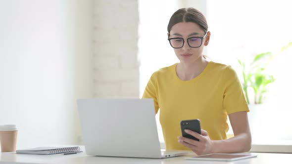 Woman Talking on Phone while using Laptop in Office alt
