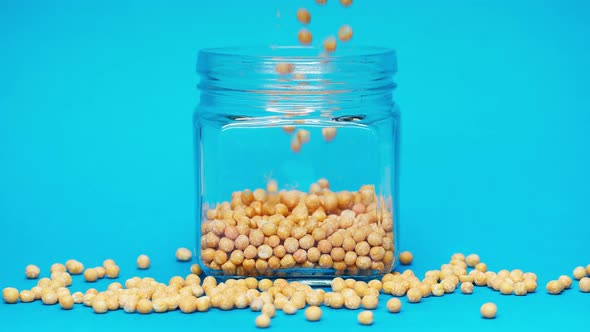 Closeup of Falling Down Peas Into Glass Jar on Blue Background alt