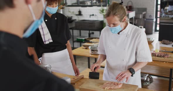 Caucasian female chef teaching diverse group wearing face masks alt