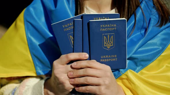 Woman Covered with the Flag of Ukraine with Ukrainian Passports in Her Hands alt