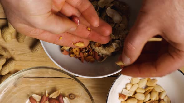 Close-up of men's hands peeling peanuts over bowls. Top view. Peeling an earthy peanut at home alt