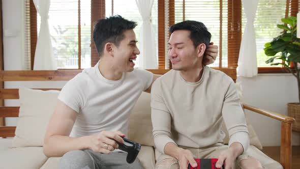 Happy asia young gay couple sit on couch use joystick controller play video game spend fun time .