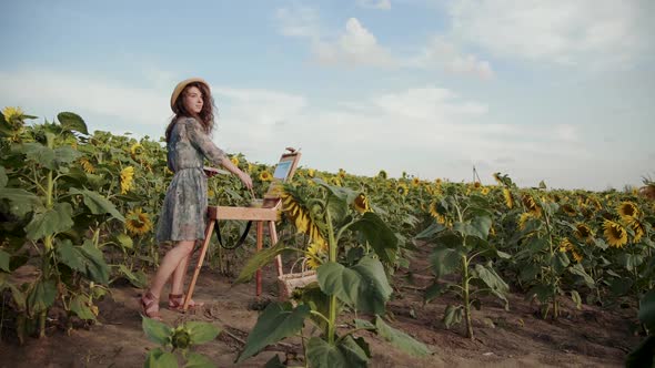 Pretty Female Artist Looking Around the Spacious Sunflower Field During Painting alt
