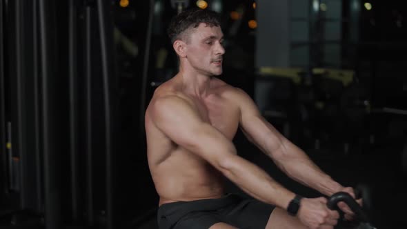 Man in the Gym Lifting Blocks on Rowing Machine Back View Training on Block Device and Gym Equipment alt