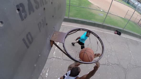 A young man basketball player dunking while playing one on one on an old outdoor basketball hoop alt