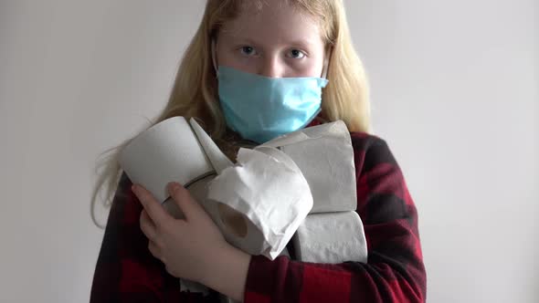 Quarantined Due To an Epidemic of Coronavirus. Masked Girl with Rolls of Toilet Paper Posing on Gray