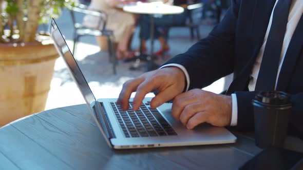 Close Up of Confident Aged Businessman Working on Laptop and Drinking Coffee in Outdoors Cafe alt