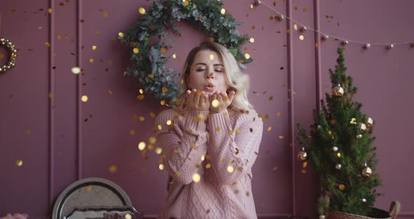 Beautiful Woman in Sweater Blows Shiny Confetti From Her Hands To the Camera in Slow Motion alt