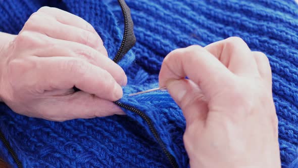 Female hands sew a zipper on a knitted blue sweater