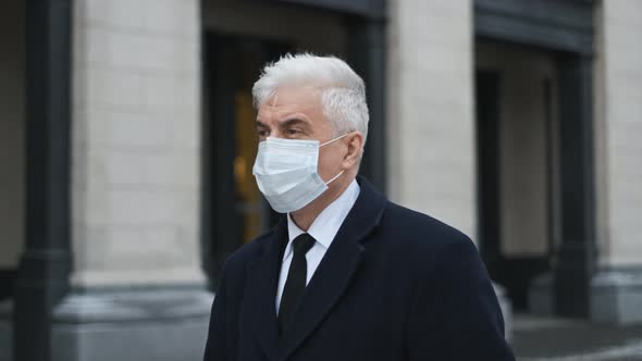 Man with Grey Hair and in Facemask Due to Pandemic Walks on Empty City Streets alt