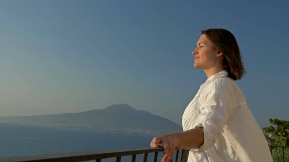 Young Woman Stands on a Balcony with a Beautiful View of the Sea and Mountains alt
