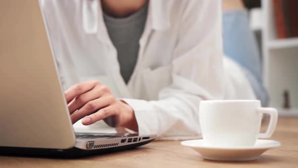 The Girl Is Working On A Laptop Laptop Lying On The Pole. A Girl Lies On A Wooden Floor At Home alt