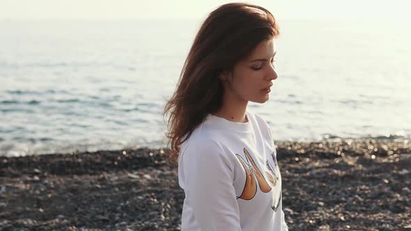 Brunette Woman Is Relaxing Alone on a Gravel Beach of Sea in Evening alt