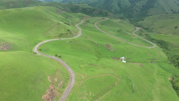 Top view of the mountain road through the green field.